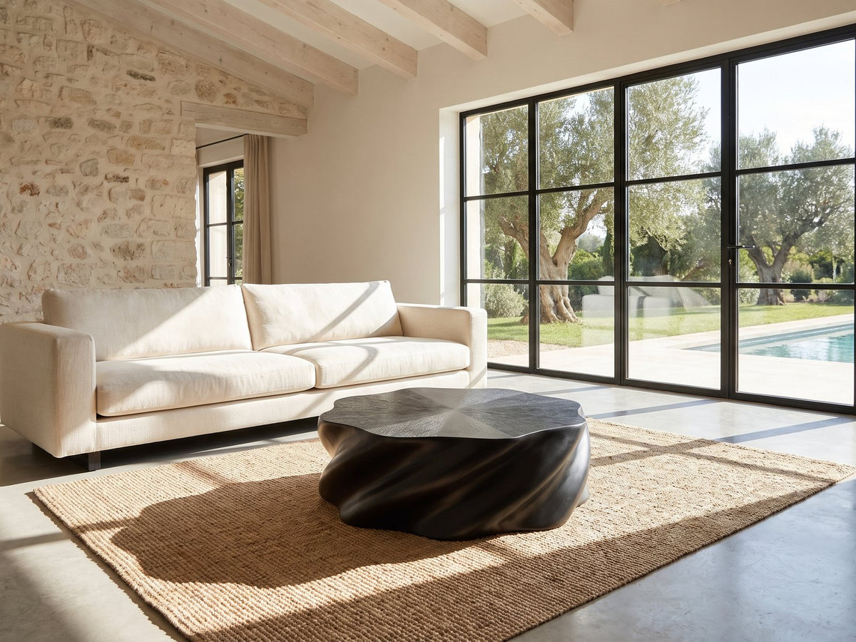 Spilimbergo Black Fiberglass Twisted Petal Coffee Table on a jute rug in front of a linen sofa in a poolside villa