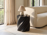 Spilimbergo Black Fiberglass Twisted Petal Side Table with a lamp and a ceramic bowl beside a cream boucle sofa in a bright plaster room