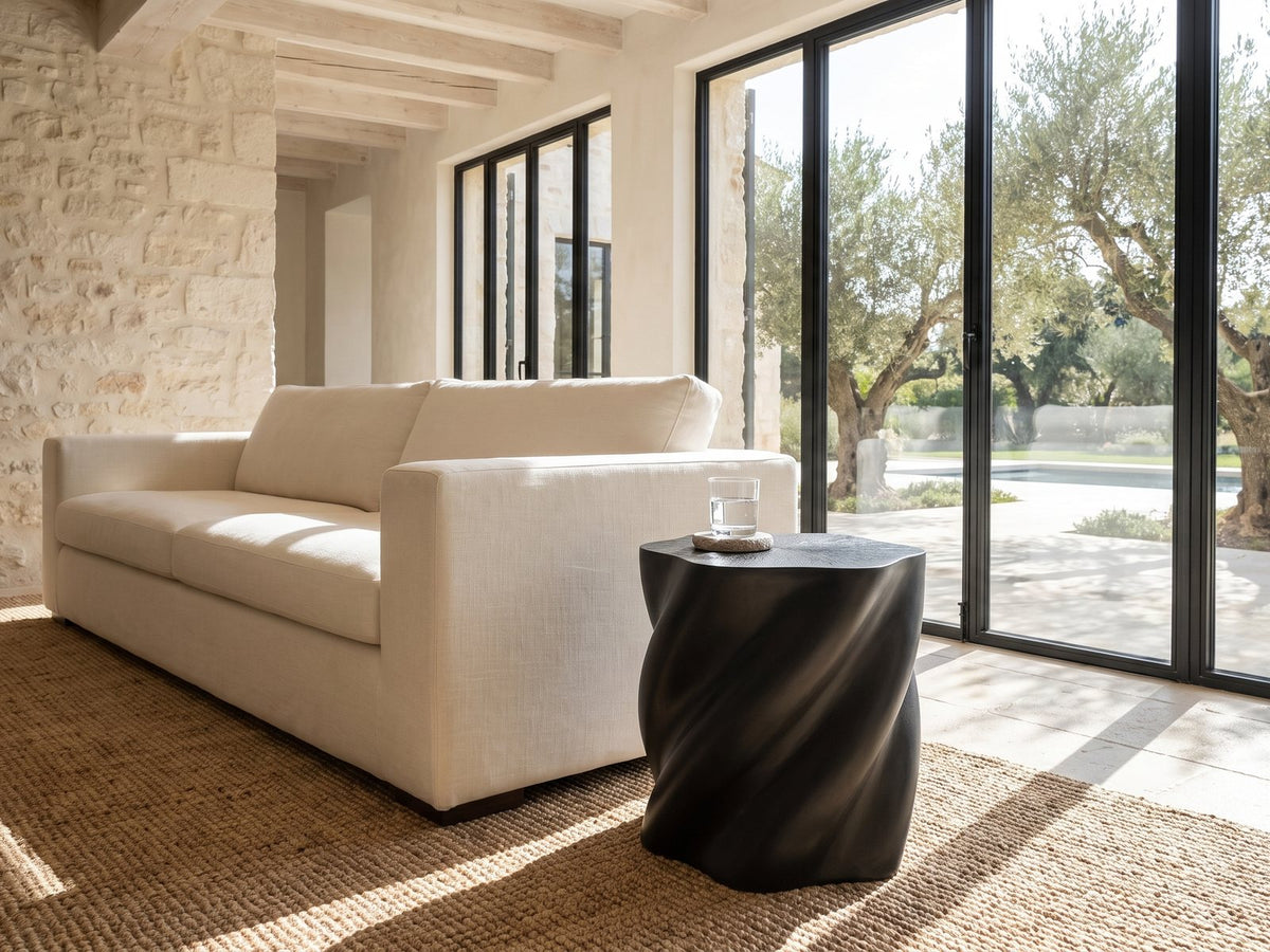 Spilimbergo Black Fiberglass Twisted Petal Side Table beside a linen sofa in a poolside villa