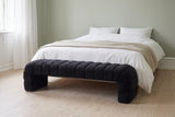 Spoleto black chenille bench at the foot of a made bed in a Copenhagen bedroom with a sage-green wall, white linen and pale oak floorboards