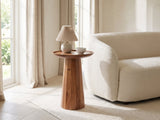Sternatia Cognac Acacia Pedestal Side Table with a lamp and a ceramic bowl beside a cream boucle armchair in a bright plaster room