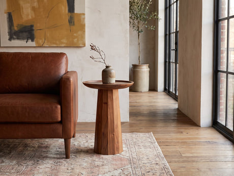 Sternatia Cognac Acacia Pedestal Side Table beside a leather sofa in an industrial loft
