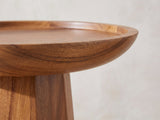 Close-up of the Sternatia Cognac Acacia Pedestal Side Table: the raised tray rim and curved underside over the faceted pedestal