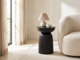 Stigliano Black Mango Bell Pedestal Side Table with a lamp and a ceramic bowl beside a cream boucle armchair in a bright plaster room