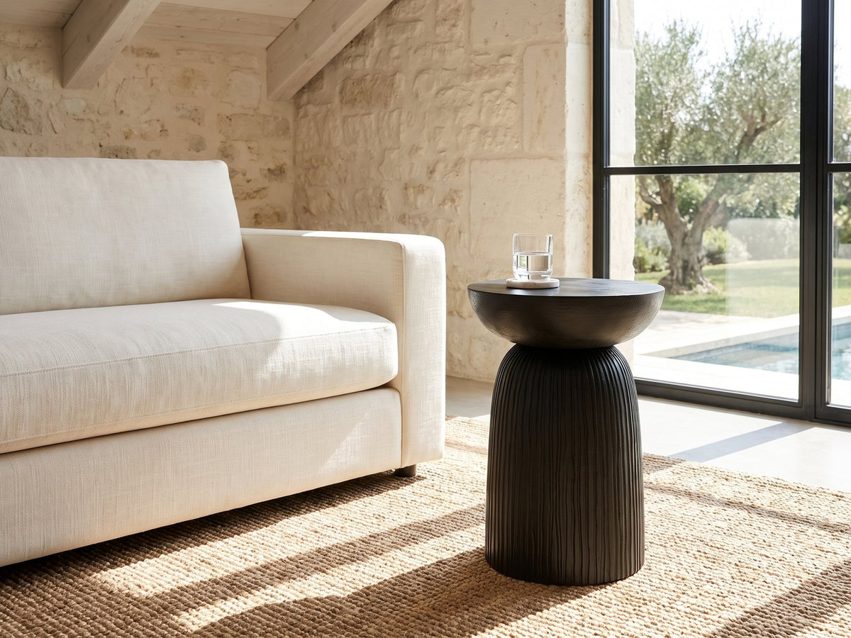 Stigliano Black Mango Bell Pedestal Side Table beside a linen sofa in a poolside villa