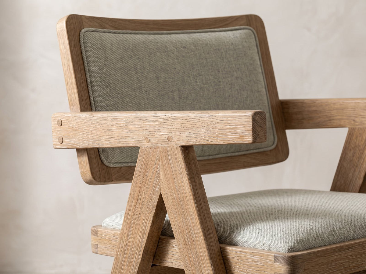 Close-up of the Stilo 84-Inch Weathered Oak Trestle Dining Set with 6 Armchairs: a Jeanneret-style armchair with plank arms and compass legs in weathered oak