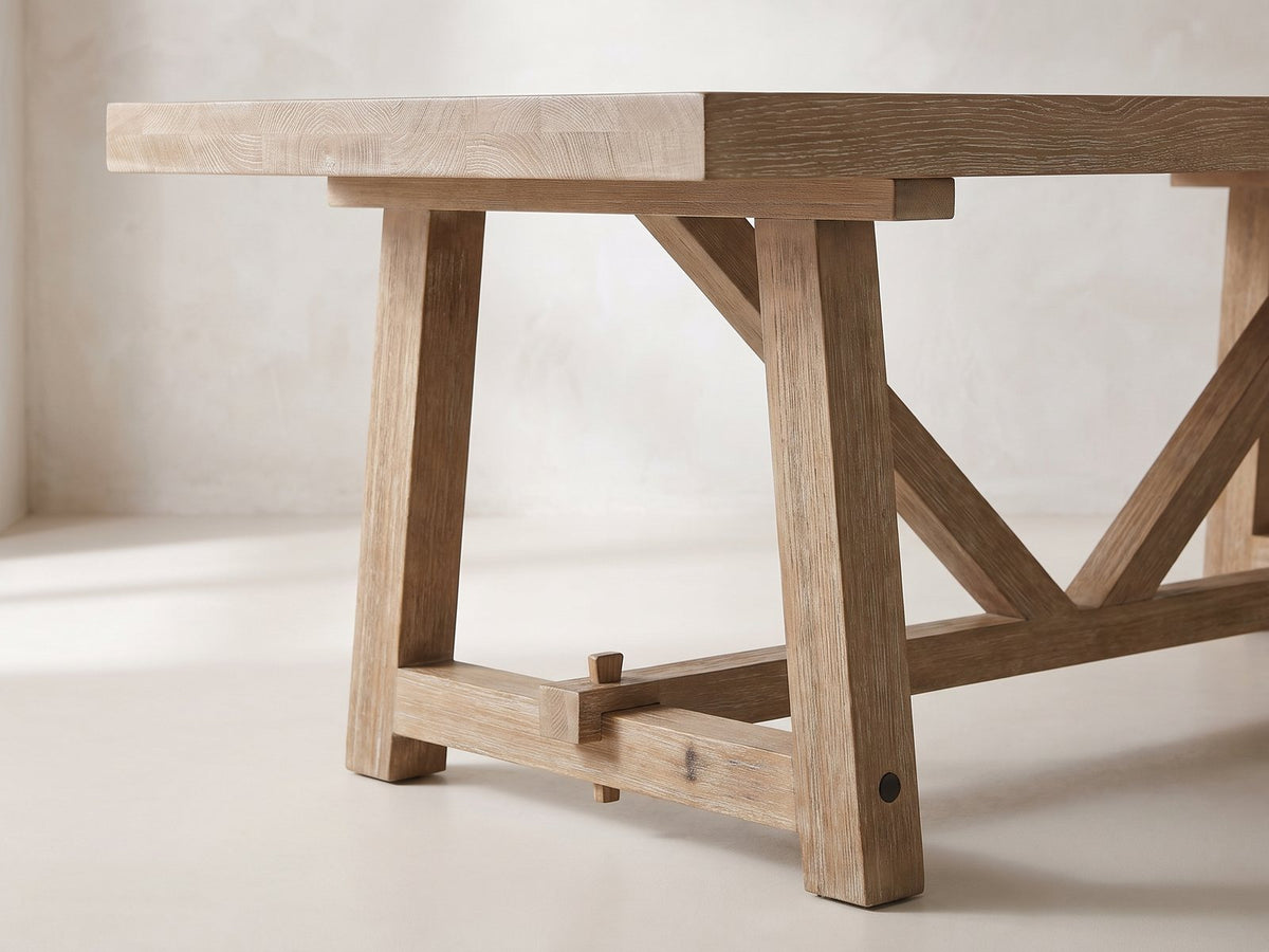Close-up of the Stilo 84-Inch Weathered Oak Trestle Dining Set with 6 Armchairs: a trestle end frame with its pegged through-tenon and diagonal brace under the thick oak top