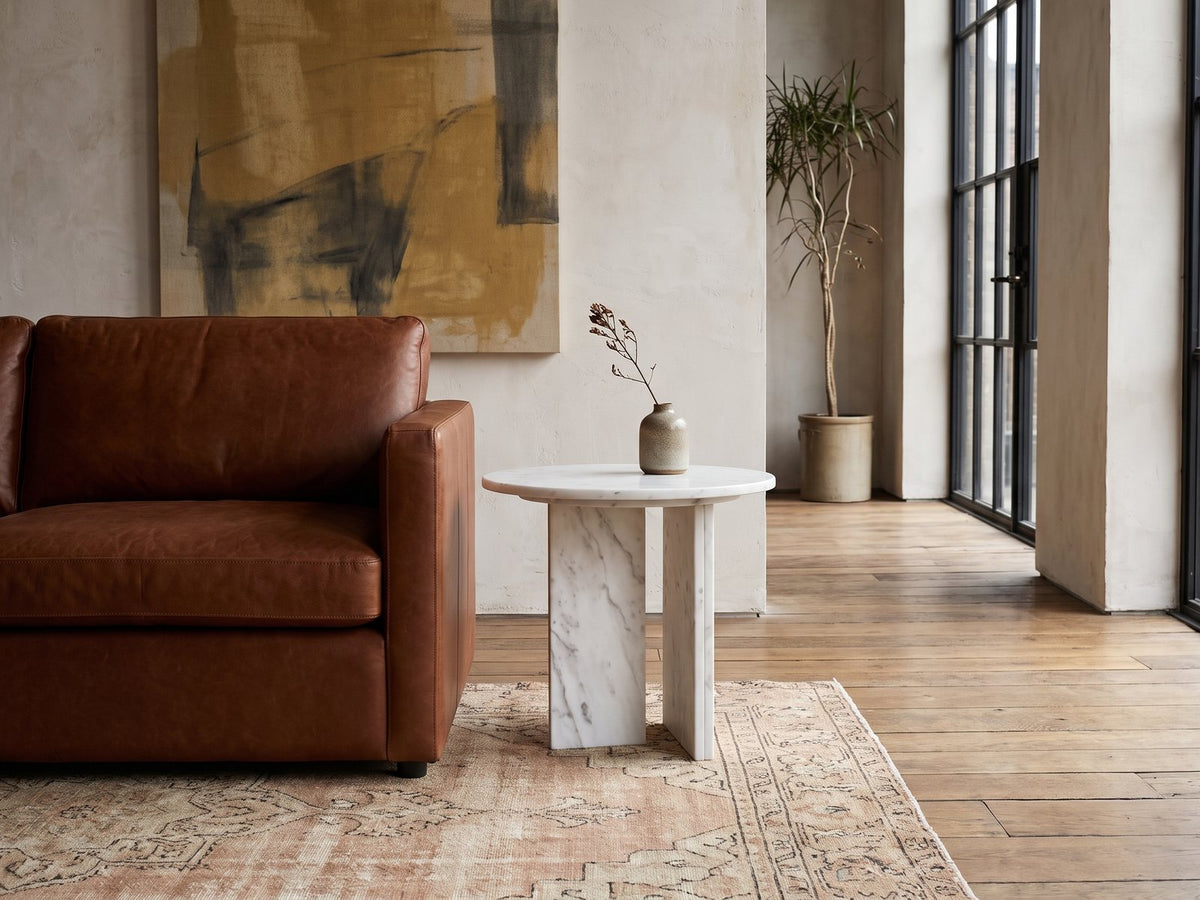 Stintino White Marble Round Side Table beside a leather sofa in an industrial loft