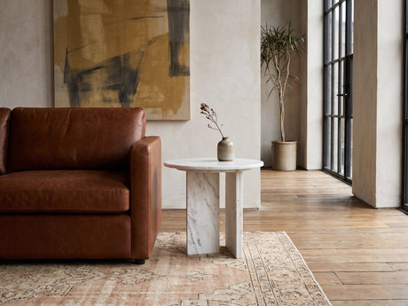 Stintino White Marble Round Side Table beside a leather sofa in an industrial loft