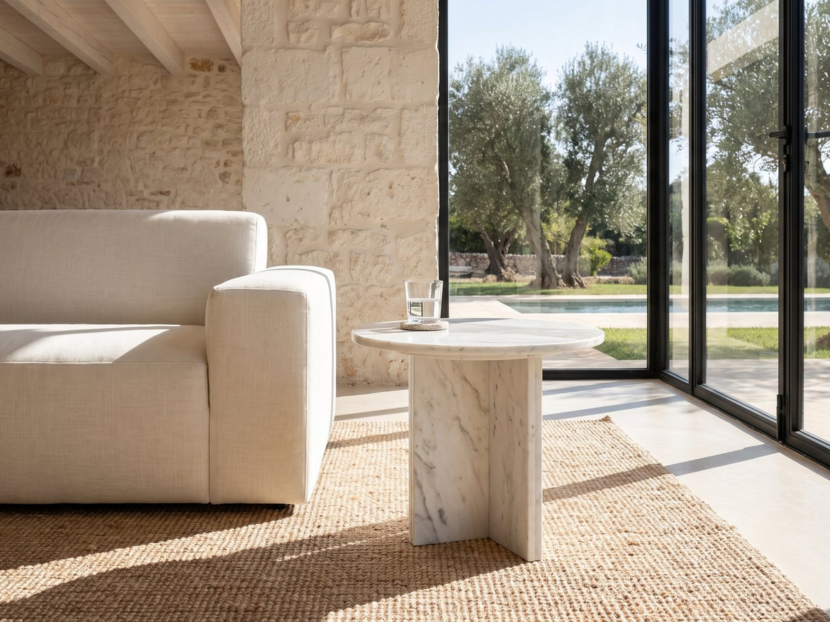 Stintino White Marble Round Side Table beside a linen sofa in a poolside villa