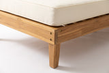 Close-up of the solid acacia on the Stromboli daybed set: the apron rail, a tapered leg and brass-coloured screw heads in light teak finish, under an ivory seat cushion