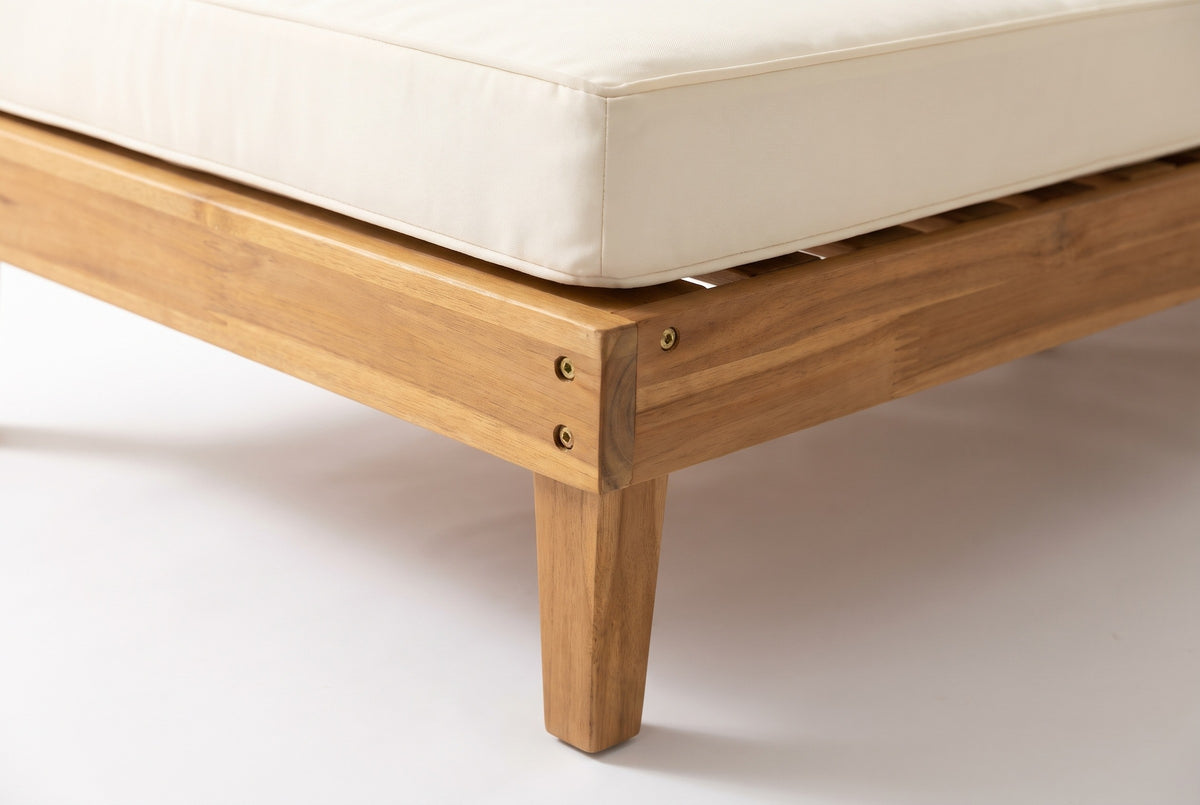 Close-up of the solid acacia on the Stromboli daybed set: the apron rail, a tapered leg and brass-coloured screw heads in light teak finish, under an ivory seat cushion