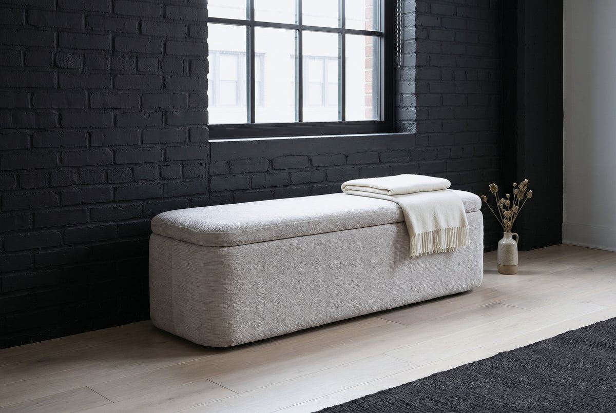 Subiaco gray storage bench under a tall steel-framed window against a charcoal-painted brick wall in a Chicago loft, with a folded off-white throw on the lid and a dried-stem vase beside it