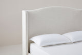 One side of the Sulmona headboard: the camelback top edge sweeping up from the shoulder to the crown, and the rounded-top wing beside the plain flat panel, above a white pillow