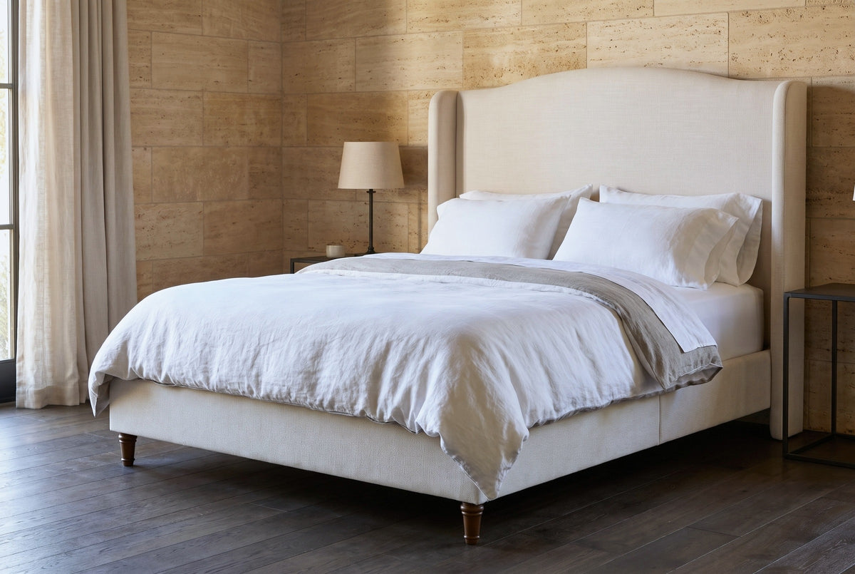 Sulmona bed against honey-coloured travertine stone walls in a Napa Valley bedroom with a dark smoked-oak floor