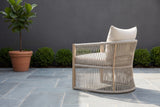 The Sutera rope lounge chair seen from behind on bluestone paving in a walled Houston courtyard, a charcoal plaster wall and boxwood behind