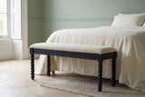 Sutri black bobbin-leg bench at the foot of a bed with ivory linen bedding in a Brooklyn brownstone bedroom with a sage green wall and a pale herringbone floor (bed not included)