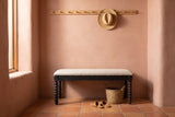 Sutri black bobbin-leg bench against a terracotta-pink adobe plaster wall in a Santa Fe entry with a saltillo tile floor, a straw hat on a peg rail, a seagrass basket and a pair of leather slippers