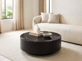 Taormina Black Marble Drum Coffee Table styled with books, a vase and a stone bowl in front of a cream sofa in a bright plaster room