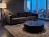 Taormina Black Marble Drum Coffee Table on a wool rug in front of a velvet sofa in a city penthouse at blue hour