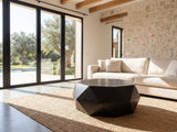 Taranto Black Faceted Drum Coffee Table on a jute rug in front of a linen sofa in a poolside villa