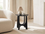 Taviano Black Wood Veneer Round Side Table with a lamp and a ceramic bowl beside a cream boucle armchair in a bright plaster room