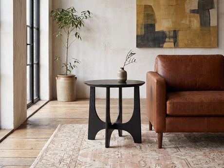 Taviano Black Wood Veneer Round Side Table beside a leather sofa in an industrial loft