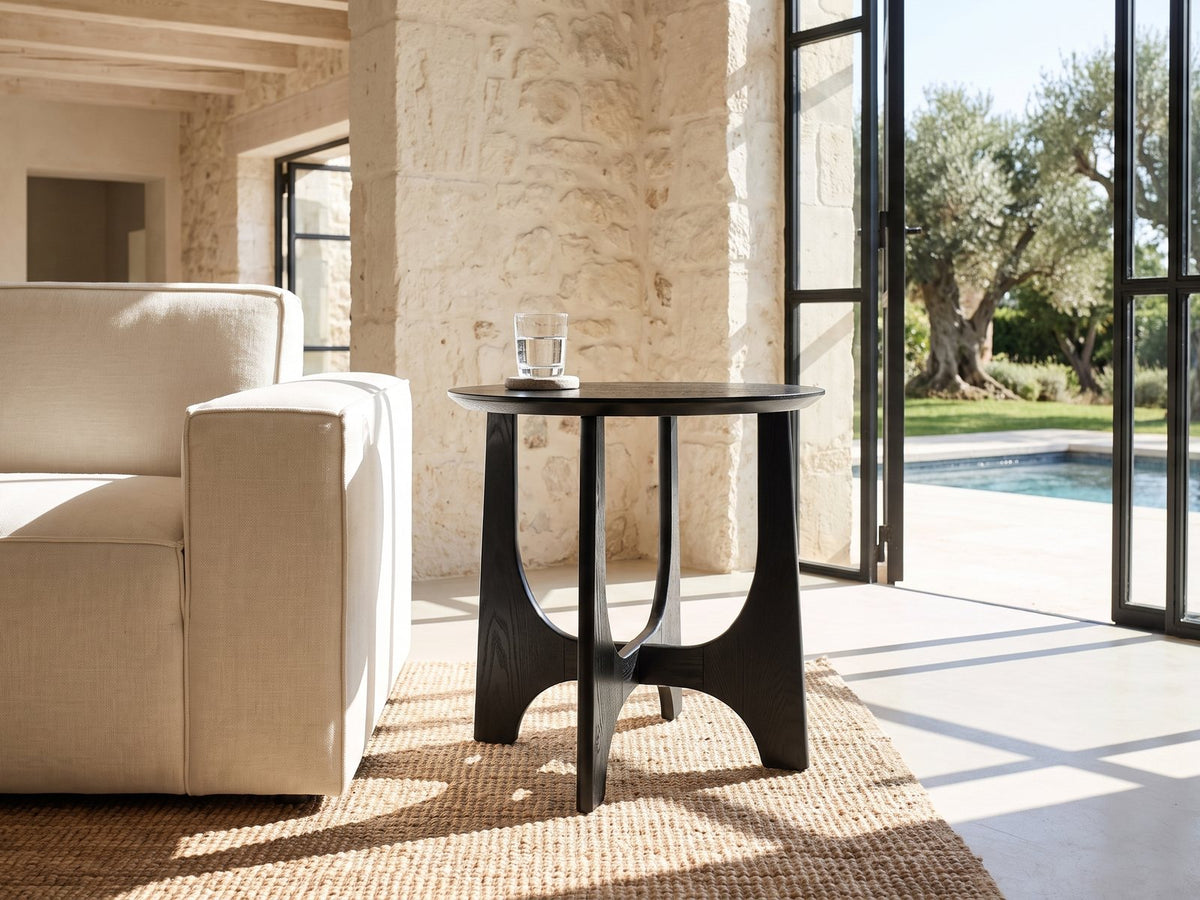 Taviano Black Wood Veneer Round Side Table beside a linen sofa in a poolside villa