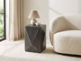 Terlizzi Graphite Cast Aluminum Faceted Side Table with a lamp and a ceramic bowl beside a cream boucle armchair in a bright plaster room