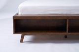 The foot of the Termoli bed: a deep walnut box with an open cubby at the end and a splayed tapered leg under the corner