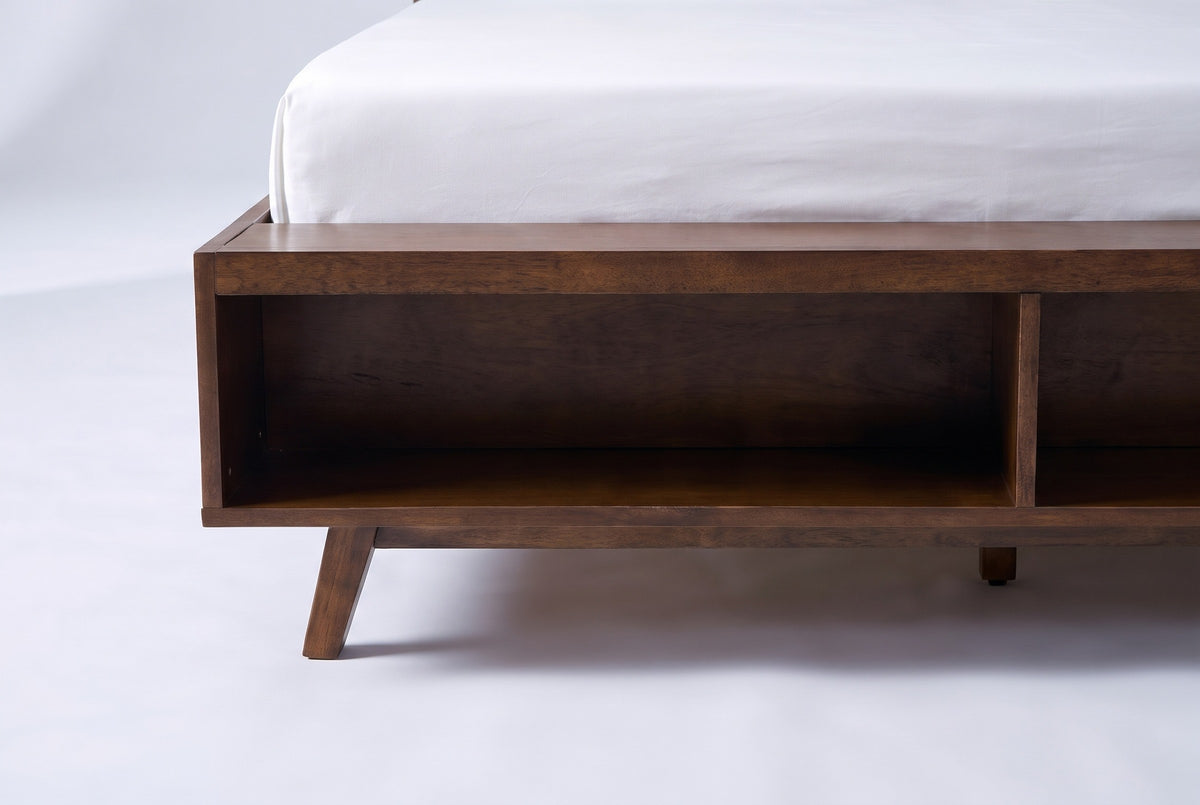 The foot of the Termoli bed: a deep walnut box with an open cubby at the end and a splayed tapered leg under the corner