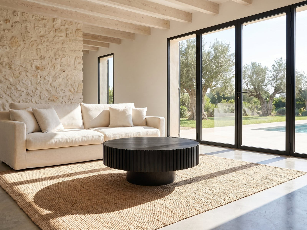 Terni Black Wood Veneer Fluted Pedestal Coffee Table seen from the side, on a jute rug in front of a linen sofa in a poolside villa