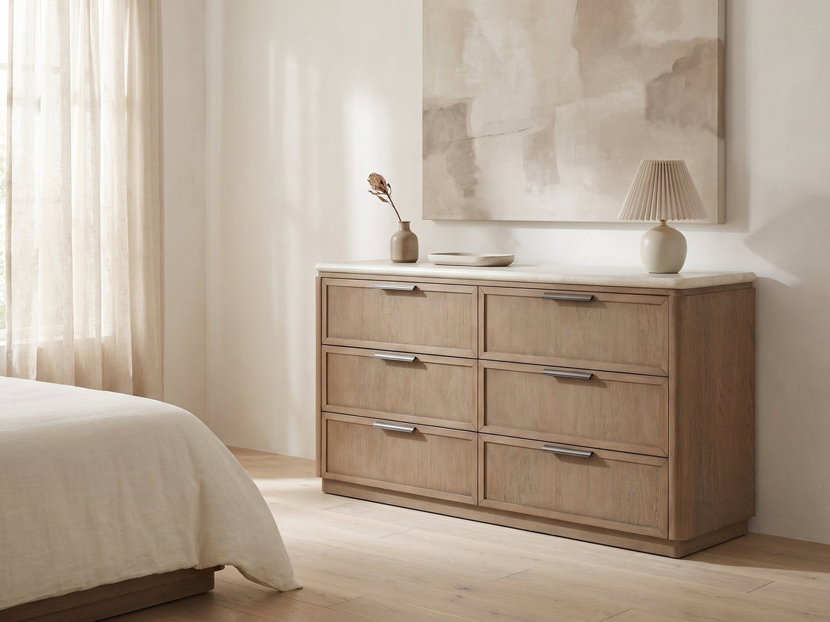 Thiene 66.5-Inch Toffee Oak Stone-Top 6-Drawer Dresser against a plaster wall under an abstract canvas in a bright bedroom