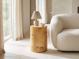 Tiriolo Natural Burl Pillar Side Table with a lamp and a ceramic bowl beside a cream boucle armchair in a bright plaster room