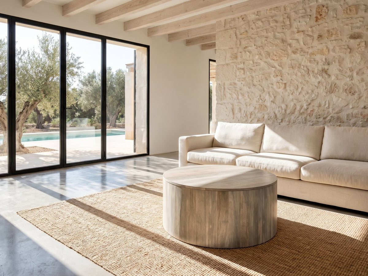 Tolentino Whitewashed Mango Drum Coffee Table on a jute rug in front of a linen sofa in a poolside villa