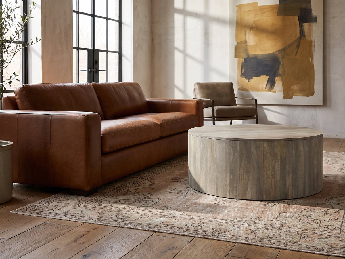 Tolentino Whitewashed Mango Drum Coffee Table on a vintage rug in front of a leather sofa in an industrial loft