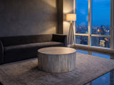 Tolentino Whitewashed Mango Drum Coffee Table on a wool rug in front of a velvet sofa in a city penthouse at blue hour