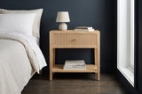 Tonara natural reeded nightstand with a ceramic lamp against a deep blue-charcoal wall in a Brooklyn bedroom