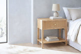 Tonara natural reeded nightstand with a ceramic lamp beside a bed in a Marfa bedroom with a pale grey microcement wall