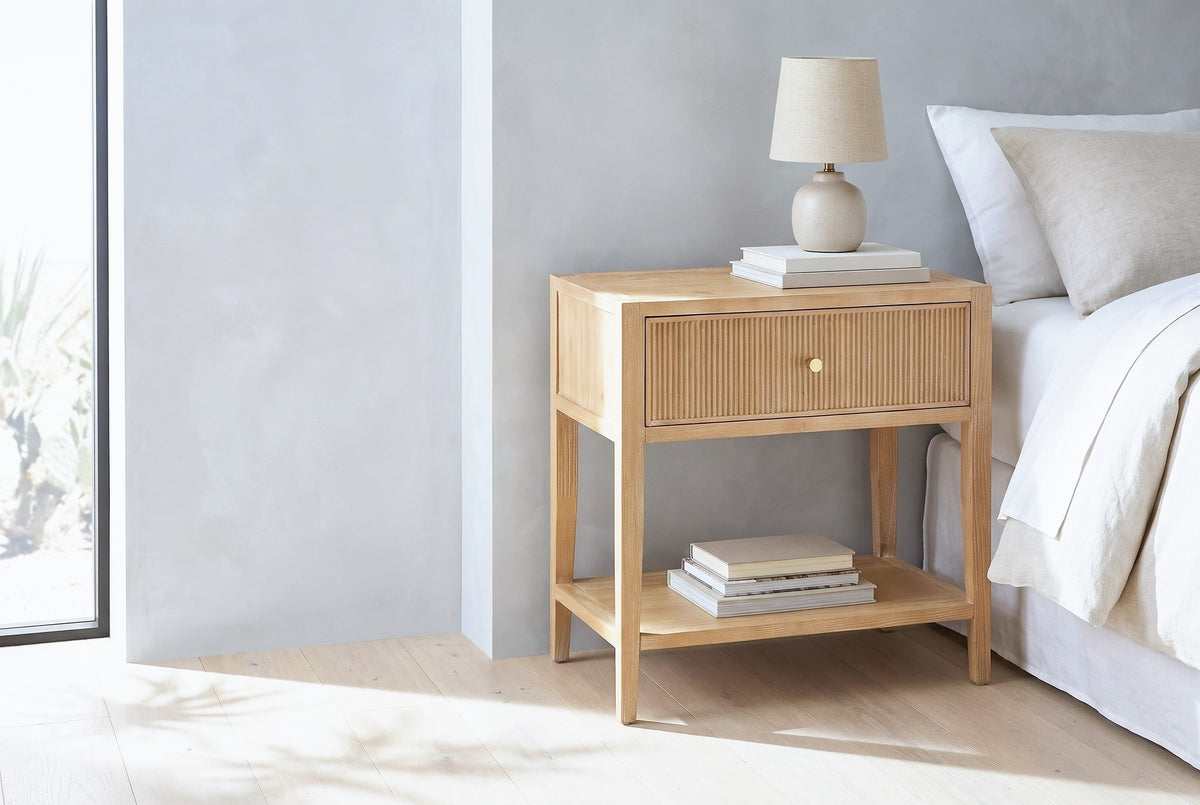 Tonara natural reeded nightstand with a ceramic lamp beside a bed in a Marfa bedroom with a pale grey microcement wall