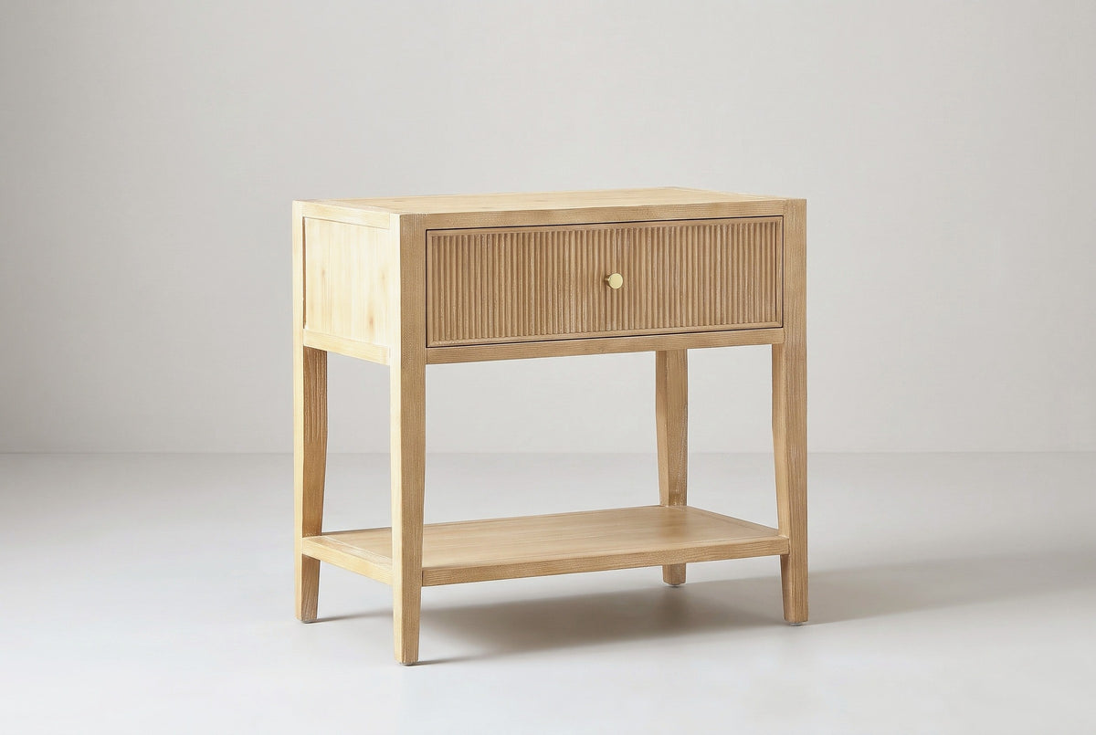 The Tonara one-drawer nightstand in light natural wood with a reeded drawer front and open lower shelf, three-quarter view on a light studio backdrop