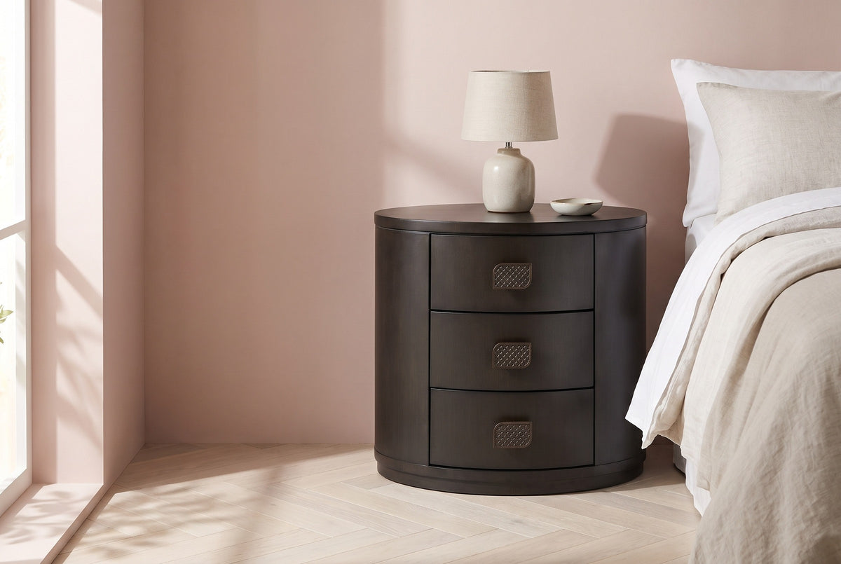 Tortoli espresso oval three-drawer nightstand with a ceramic lamp beside a bed in a Brooklyn bedroom with a blush pink plaster wall