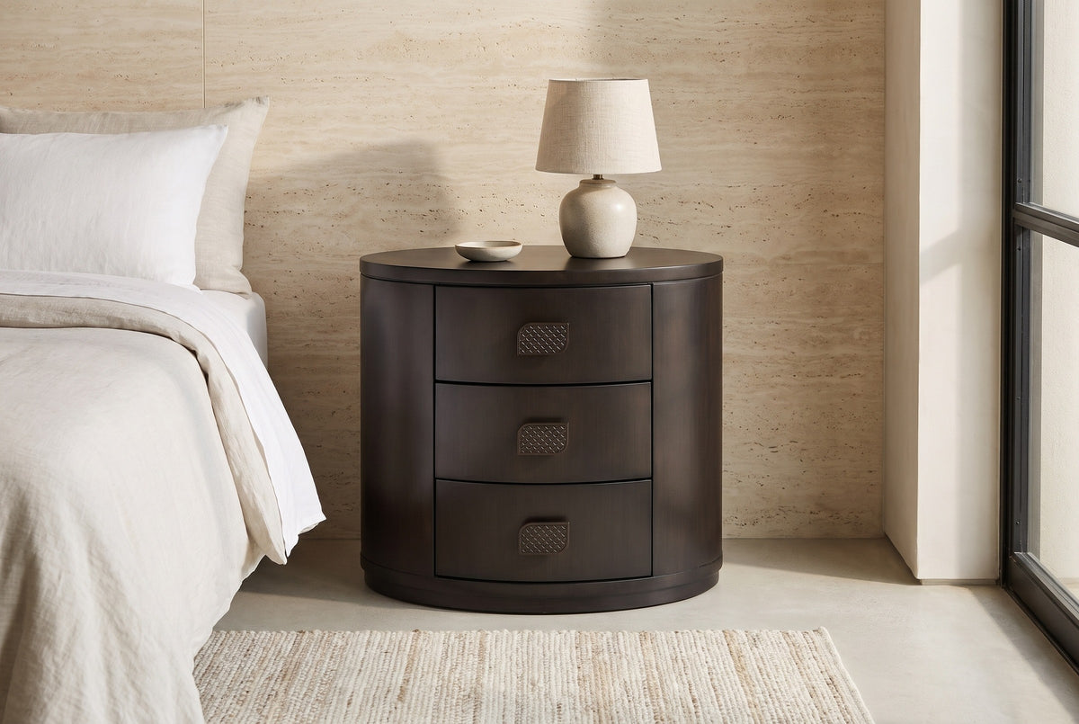 Tortoli espresso oval nightstand with a ceramic lamp against a cream travertine wall in a Phoenix bedroom