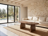 Tortona 47-Inch Oval Walnut-Finish Wood Veneer Coffee Table on a jute rug in front of a linen sofa in a poolside villa