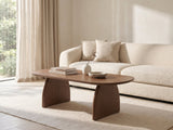 Tortona 47-Inch Oval Walnut-Finish Wood Veneer Coffee Table styled with books, a vase and a stone bowl in front of a cream sofa in a bright plaster room