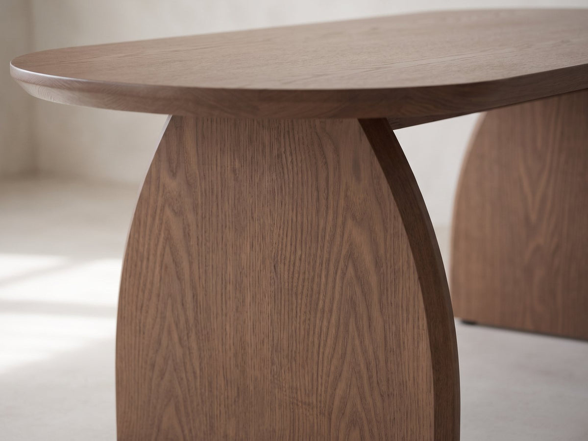 Close-up of the Tortona 47-Inch Oval Walnut-Finish Wood Veneer Coffee Table: the arched slab leg meeting the bevelled edge of the oval top