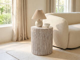 Tortora Carved Whitewash Drum Side Table with a lamp and a ceramic bowl beside a cream boucle armchair in a bright plaster room