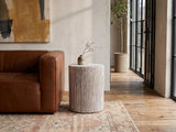 Tortora Carved Whitewash Drum Side Table beside a leather sofa in an industrial loft