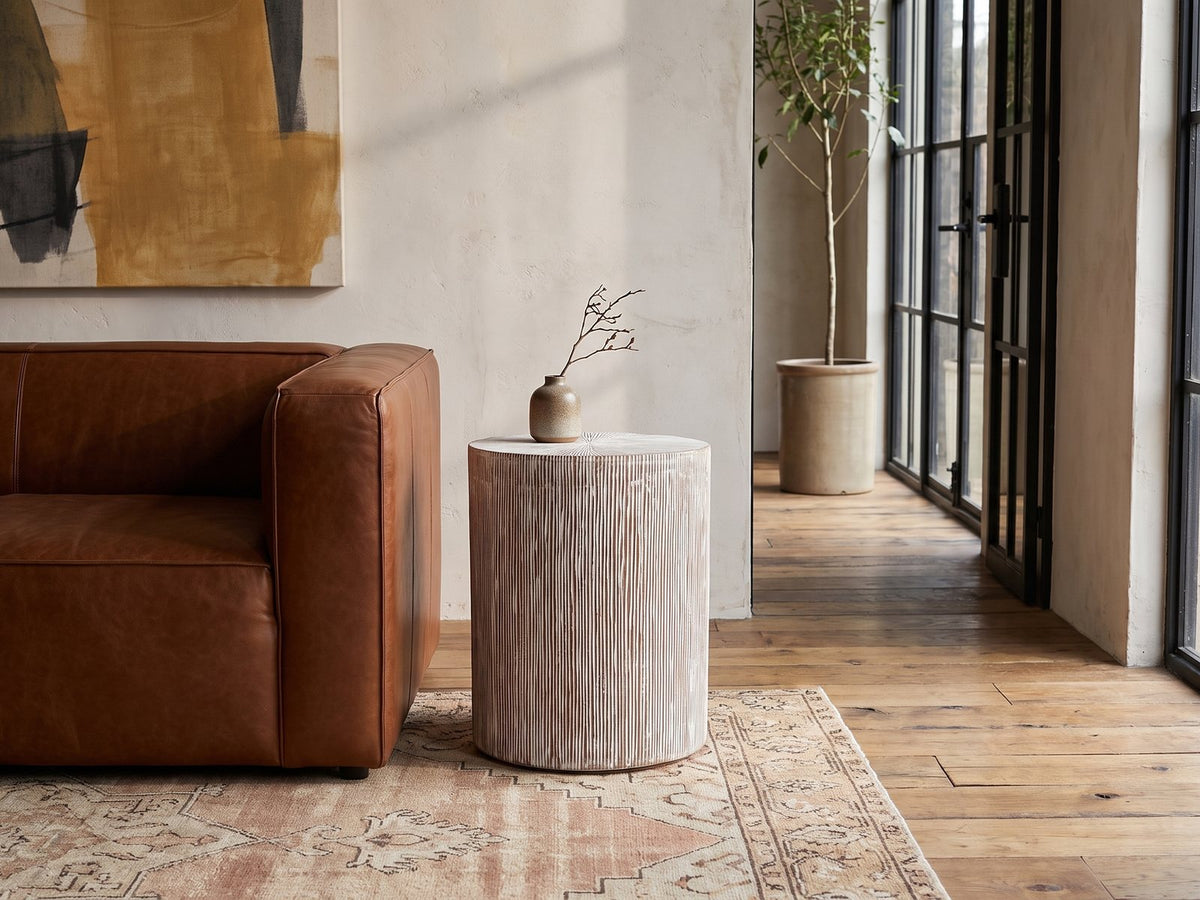Tortora Carved Whitewash Drum Side Table beside a leather sofa in an industrial loft