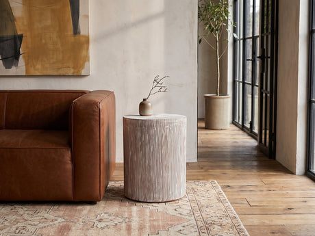Tortora Carved Whitewash Drum Side Table beside a leather sofa in an industrial loft